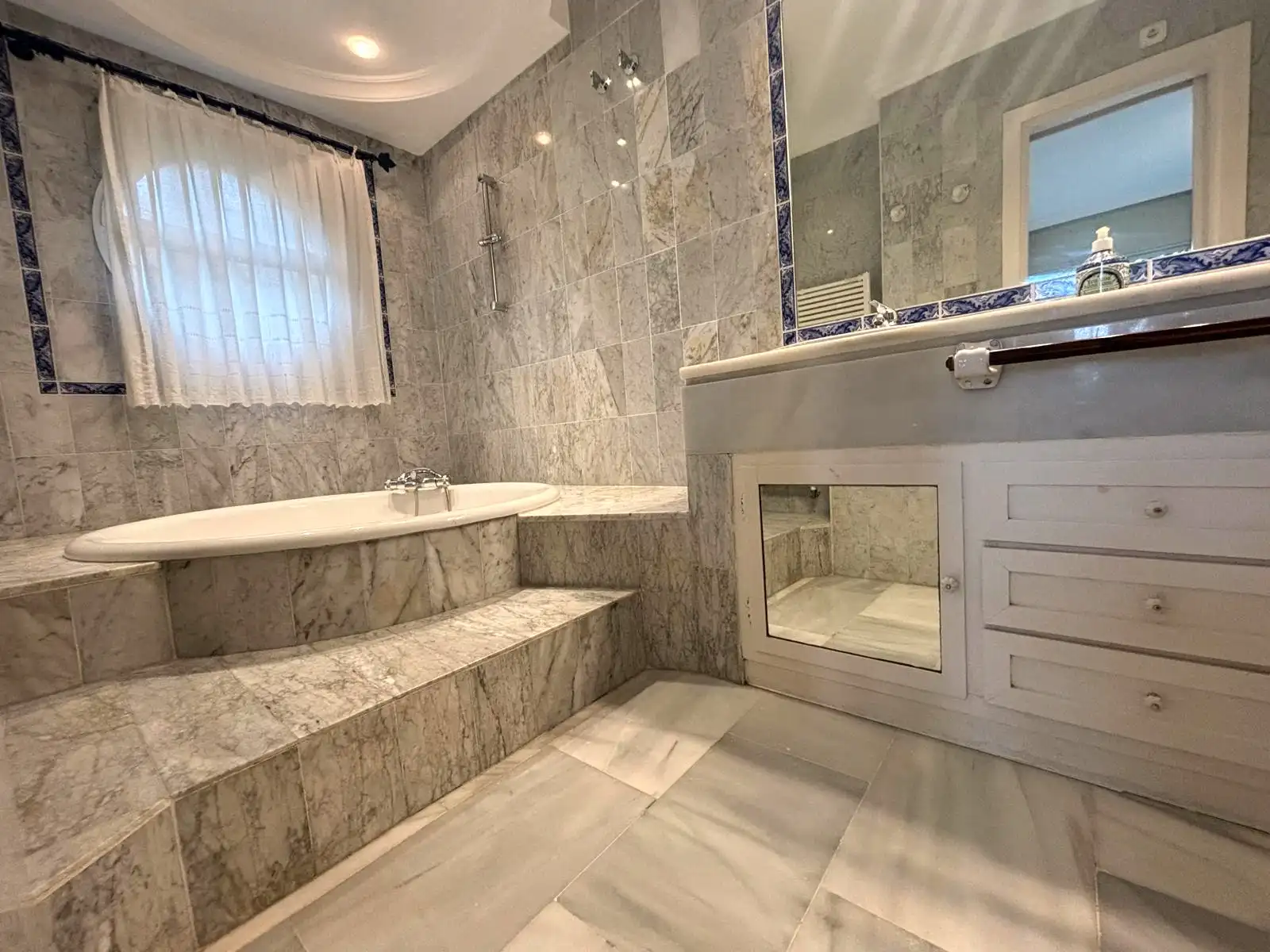 Baño principal con bañera encastrada, doble lavabo y ventana exterior en Brisas II, Manilva.