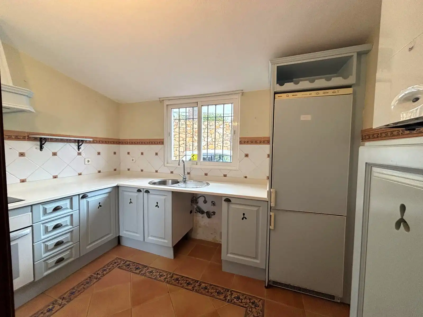 Cocina independiente con ventana exterior, fregadero bajo la ventana y mobiliario claro.