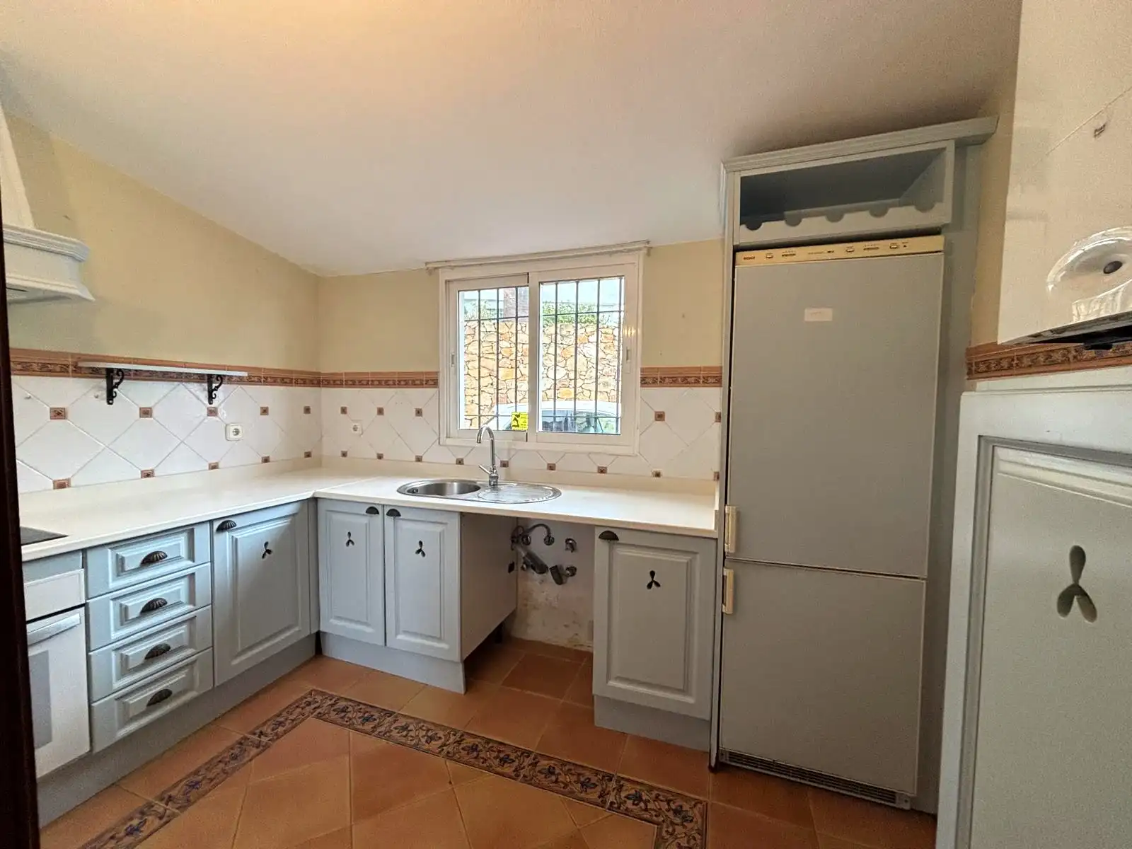 Cocina independiente con ventana exterior, fregadero bajo la ventana y mobiliario claro.