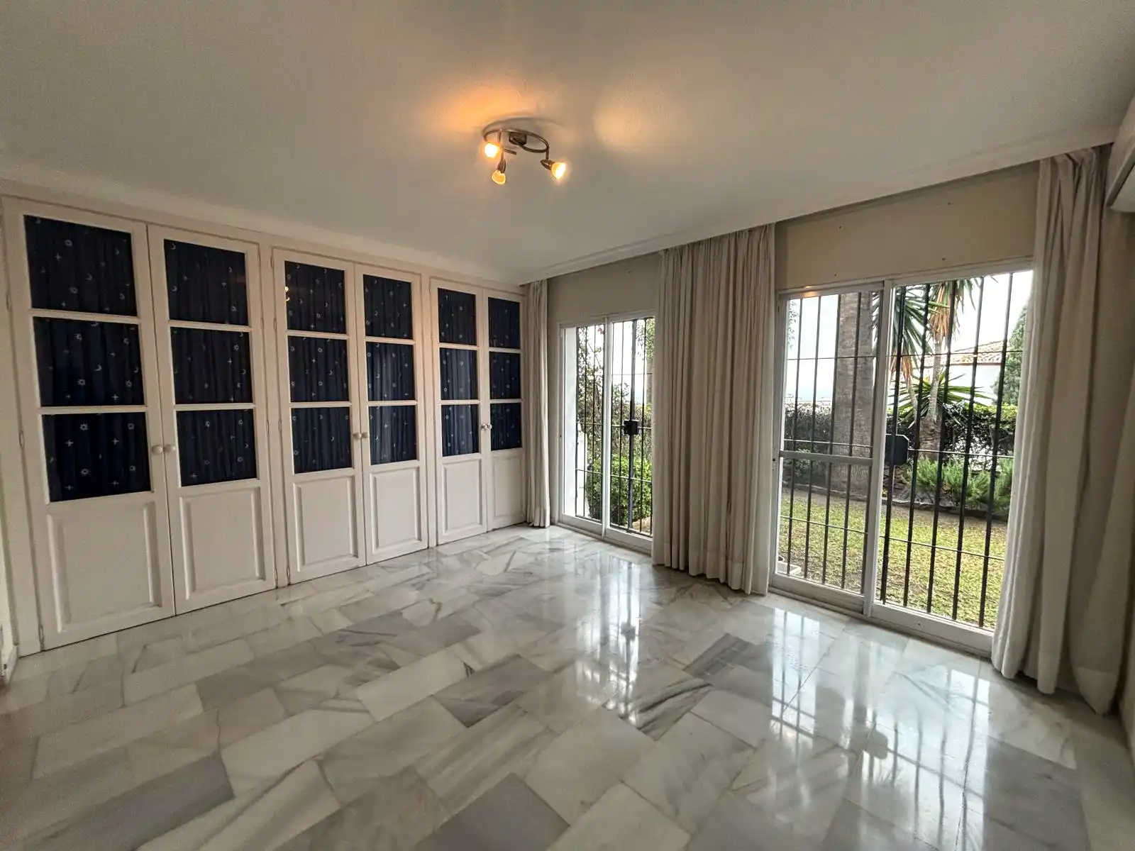 Dormitorio con armarios de pared a pared y grandes ventanales hacia el jardín en Brisas II, Manilva.