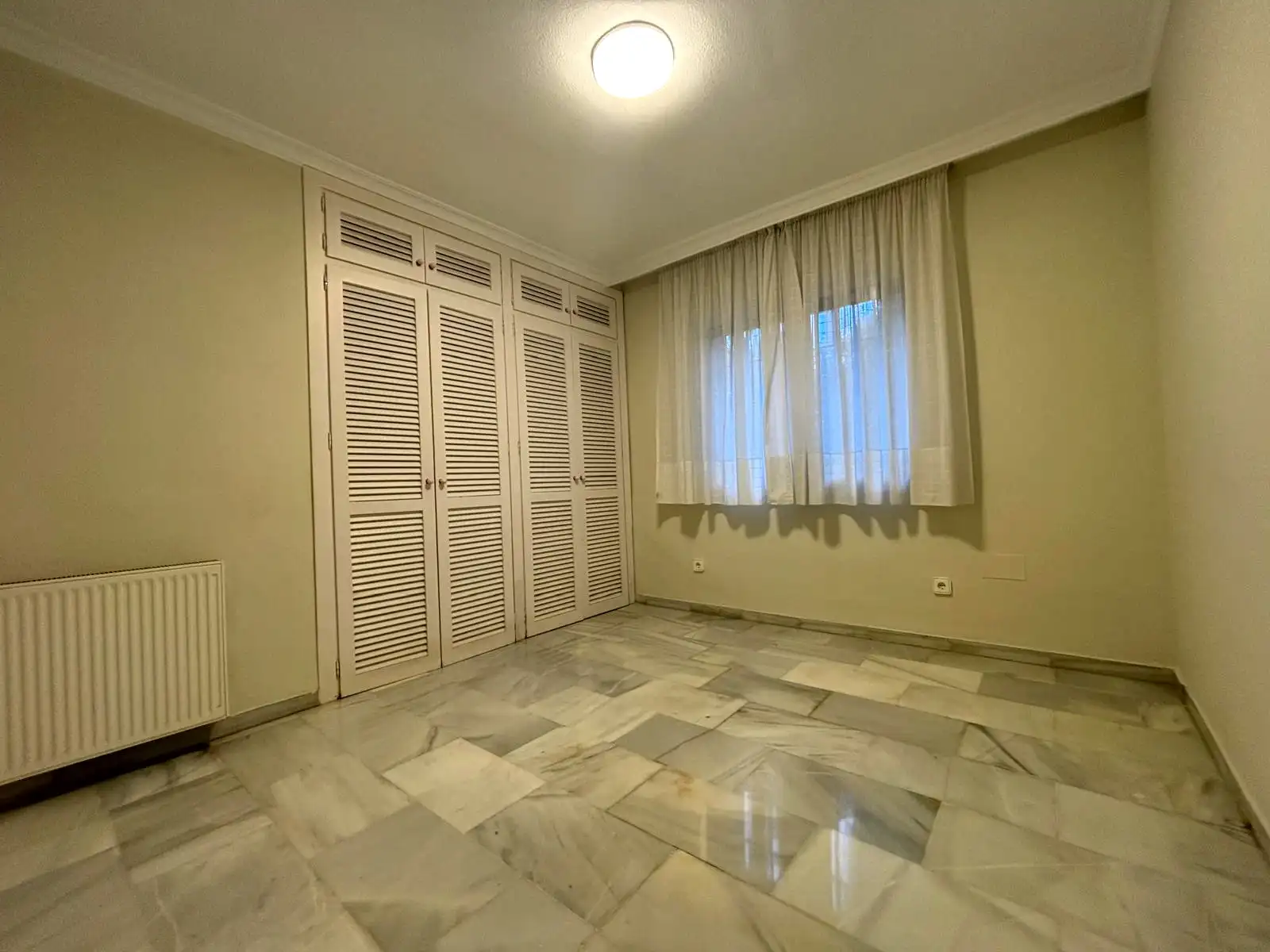 Dormitorio con armarios de lamas, ventana exterior y suelo de mármol en Brisas II, Manilva.