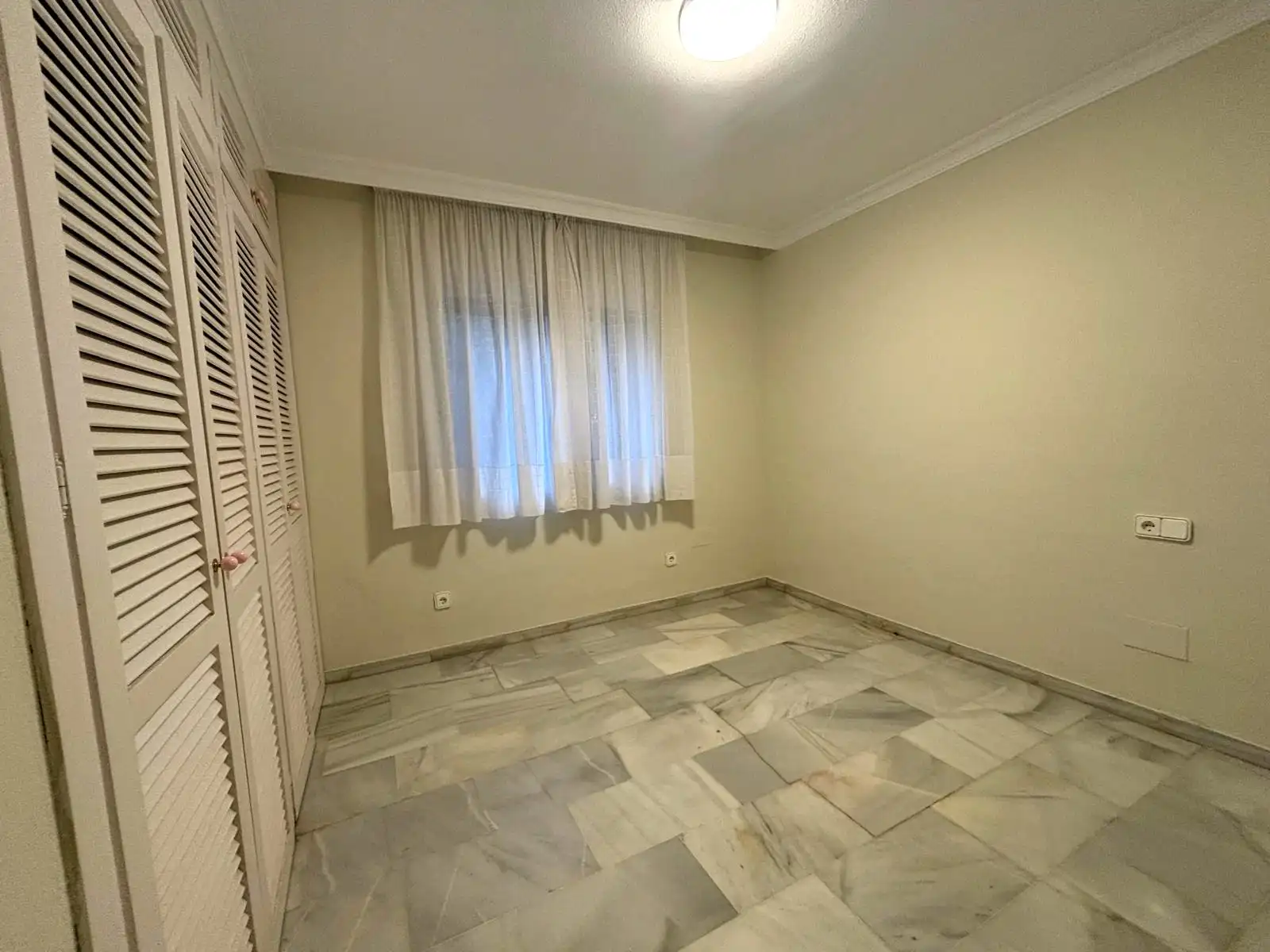 Dormitorio con armarios, ventana exterior y suelo de mármol en Brisas II, Manilva.