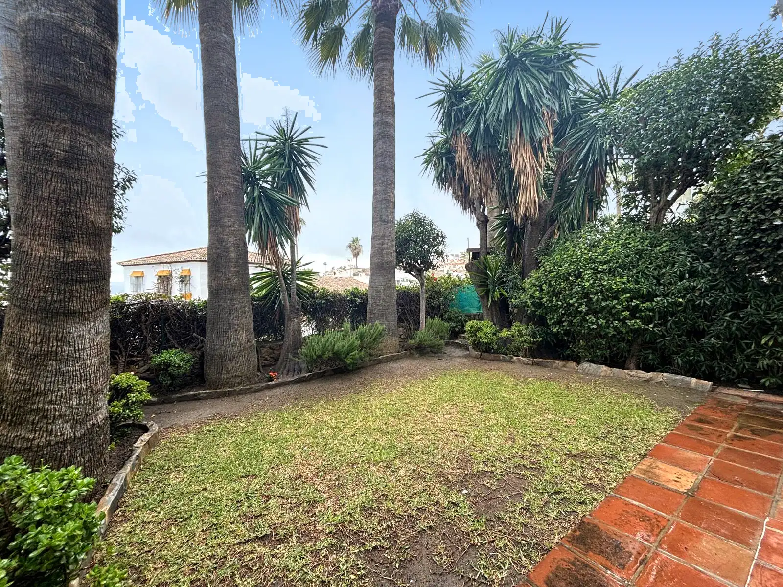 Jardín privado con césped, palmeras y solado cerámico junto a la terraza en Brisas II, Manilva.