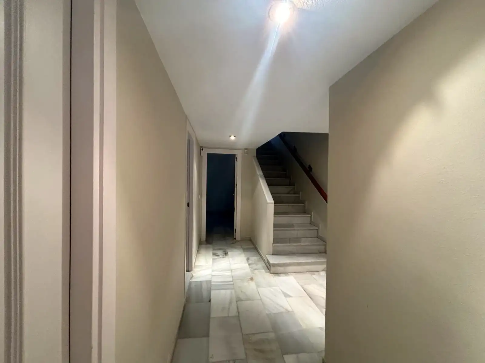 Pasillo interior con escalera, suelos de mármol y transición hacia la zona de dormitorios.