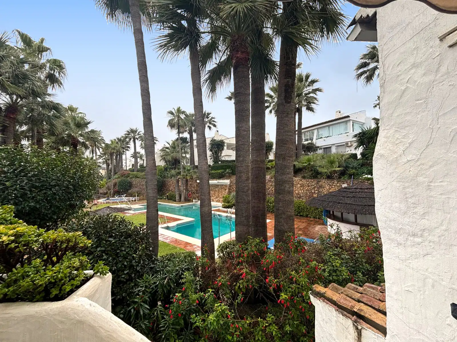 Piscina comunitaria rodeada de jardines y palmeras en la urbanización Brisas II, Manilva.