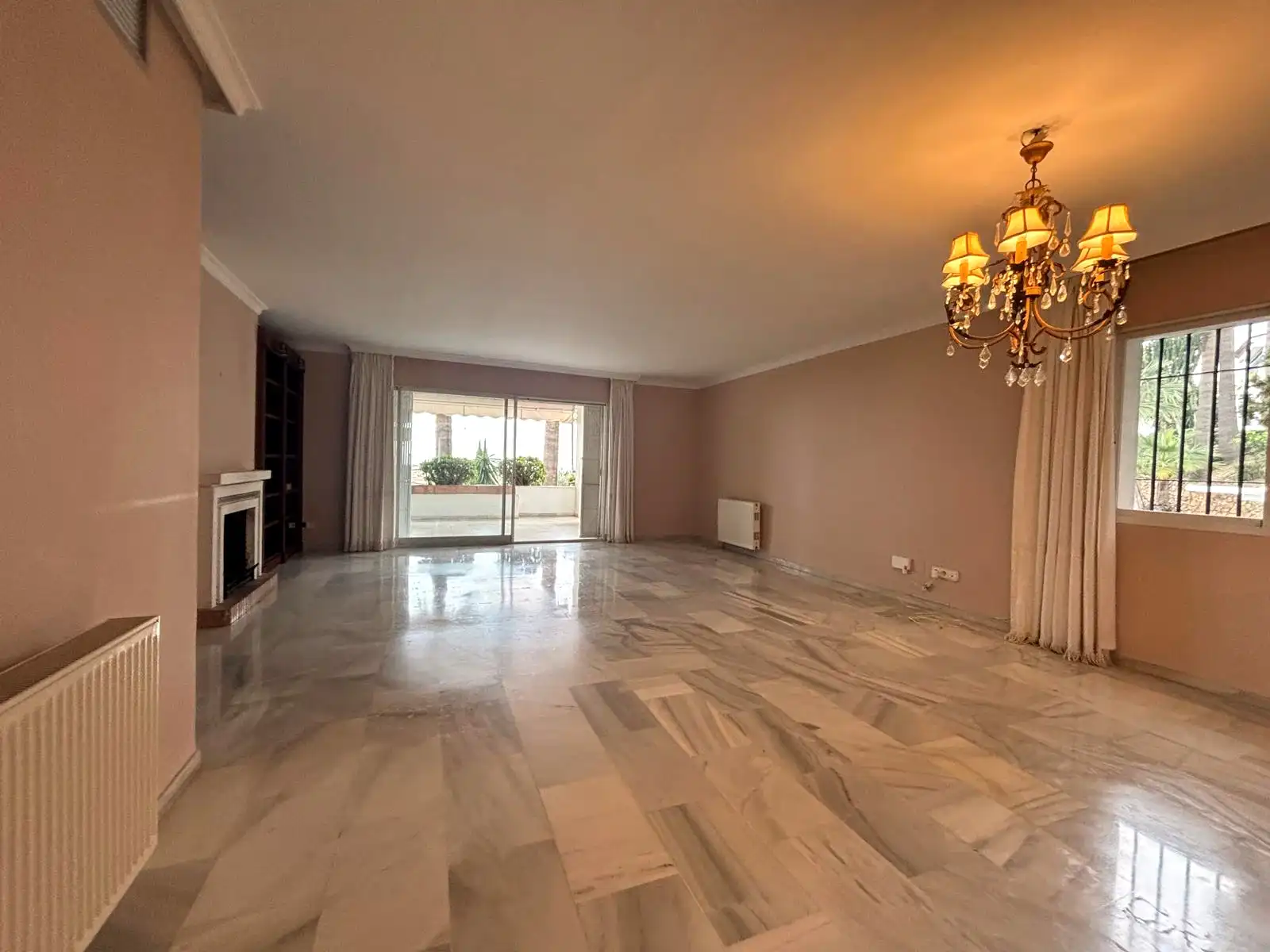 Amplio salón-comedor con suelos de mármol, chimenea y vistas hacia la terraza cubierta en Brisas II, Manilva.