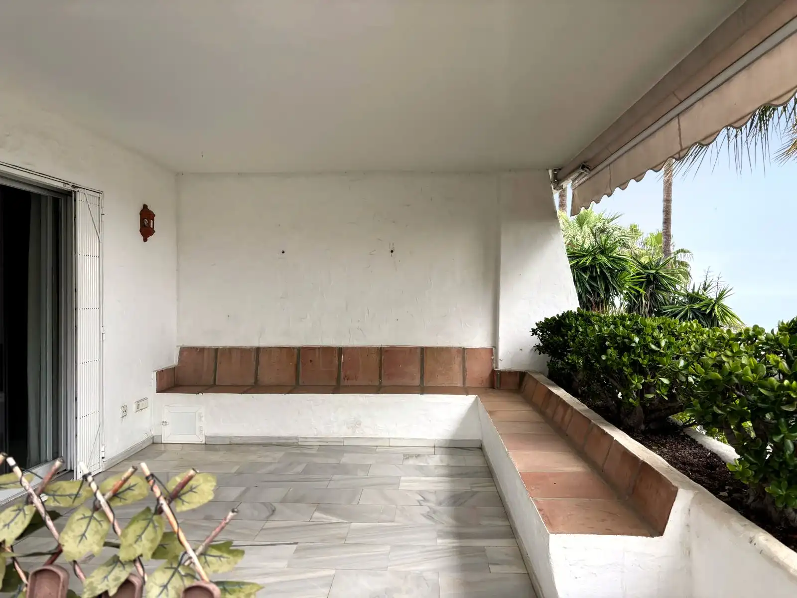 Terraza cubierta con bancos de obra y vistas abiertas al jardín y a la vegetación de Brisas II, Manilva.